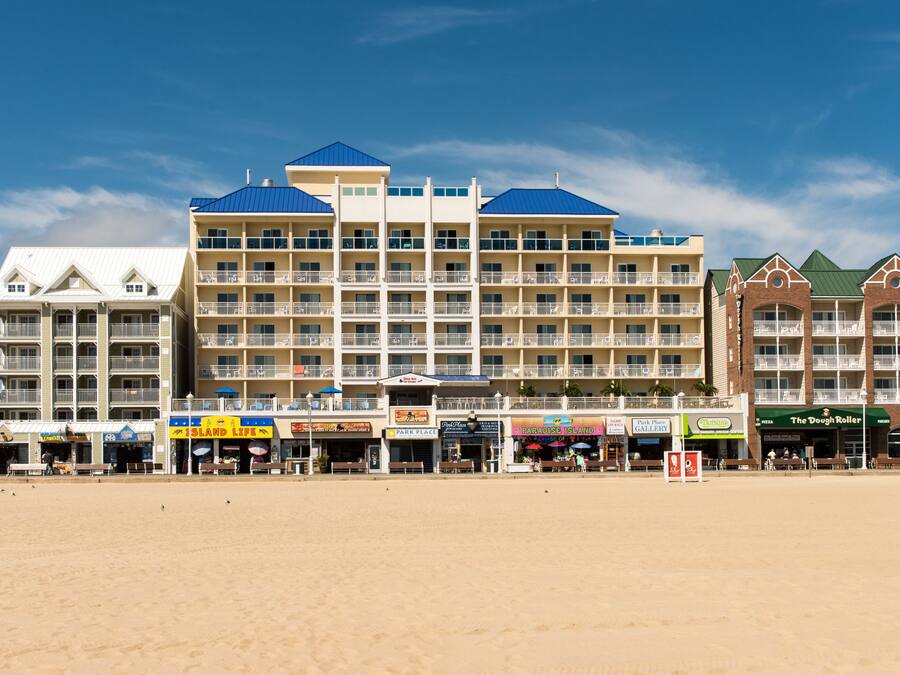 A beachfront hotel with multiple balconies, a beachside restaurant, and a boardwalk with shops.