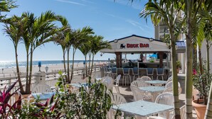 Een terras met tafels en stoelen, met uitzicht op een strand.