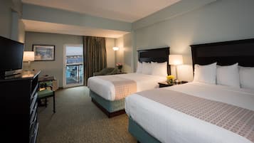 A hotel room with two beds, a desk with a TV, a chair, and a view of the sea.