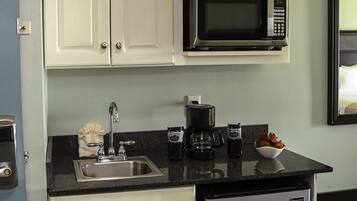 Una cocina compacta con armarios blancos, un microondas negro, una cafetera y un refrigerador.
