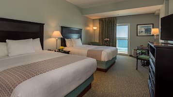 Une chambre d’hôtel avec deux lits, un bureau, une chaise, une télévision et une vue sur l’océan.