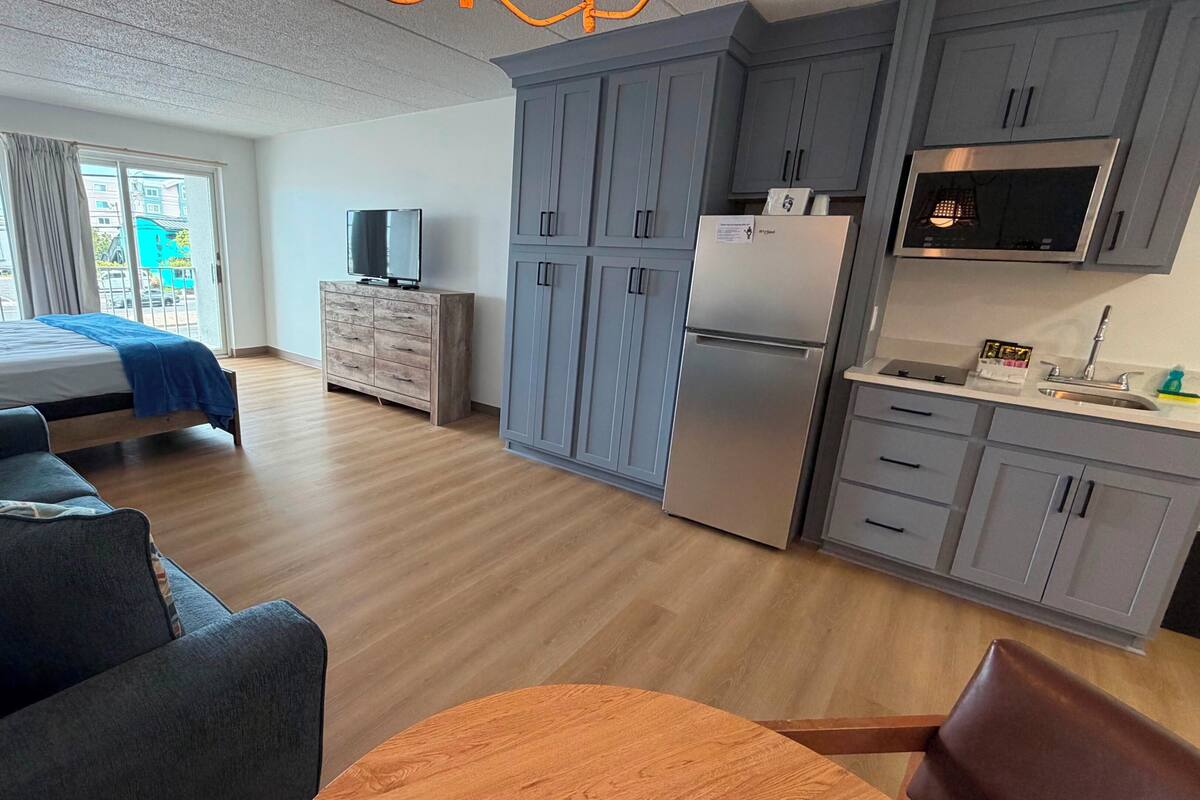 Ein modernes Hotelzimmer mit Bett, Sofa, Fernseher, Küchenzeile und Blick nach außen.
