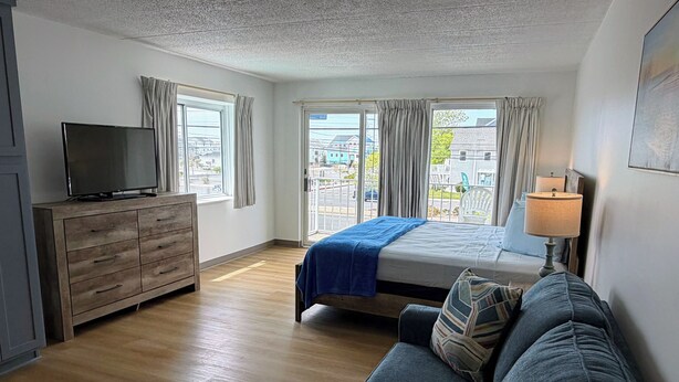 A bedroom with a bed, a TV on a wooden dresser, a sofa, and a window with curtains.
