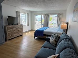 A bedroom with a bed, a TV on a wooden dresser, a sofa, and a window with curtains.
