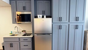 A kitchen with grey cabinets, a stainless steel refrigerator, a microwave, and a sink.