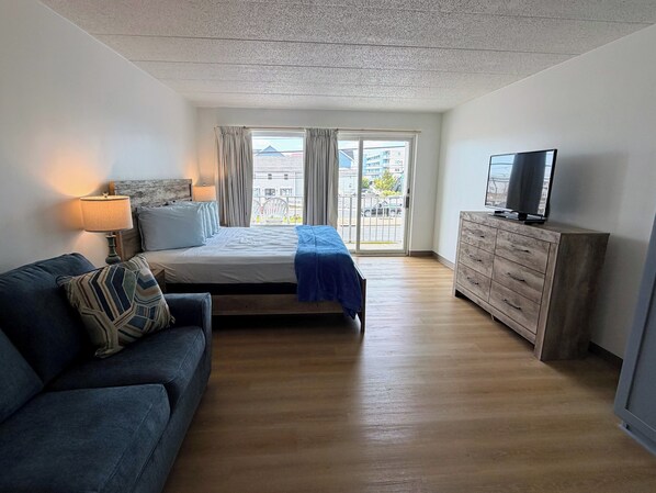 A bedroom with a bed, a TV, a dresser, a sofa, and a window with curtains.
