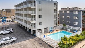 A multi-story hotel with balconies, a swimming pool, and a parking lot.