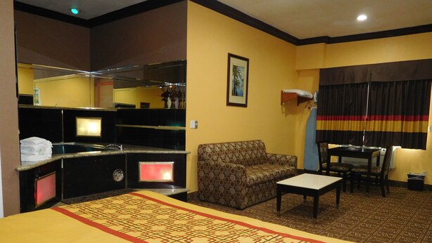 A hotel room with a bed, a sofa, a dining table, a small table, a mirror, and a window with curtains.