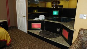 A hotel room with a bathroom featuring a large mirror, a sink, and a toilet. There is a patterned carpet on the floor and a bed with a yellow cover.