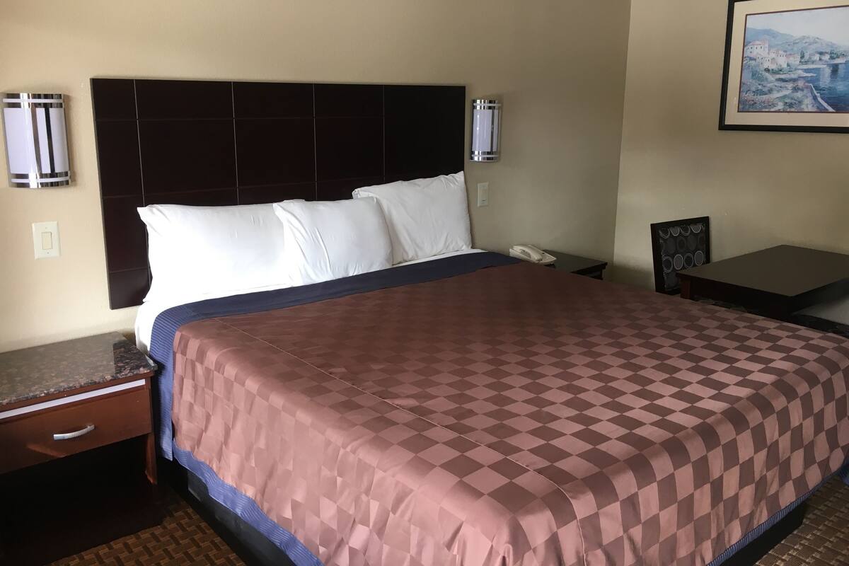 A hotel room with a large bed, a nightstand, a phone, and a painting on the wall.