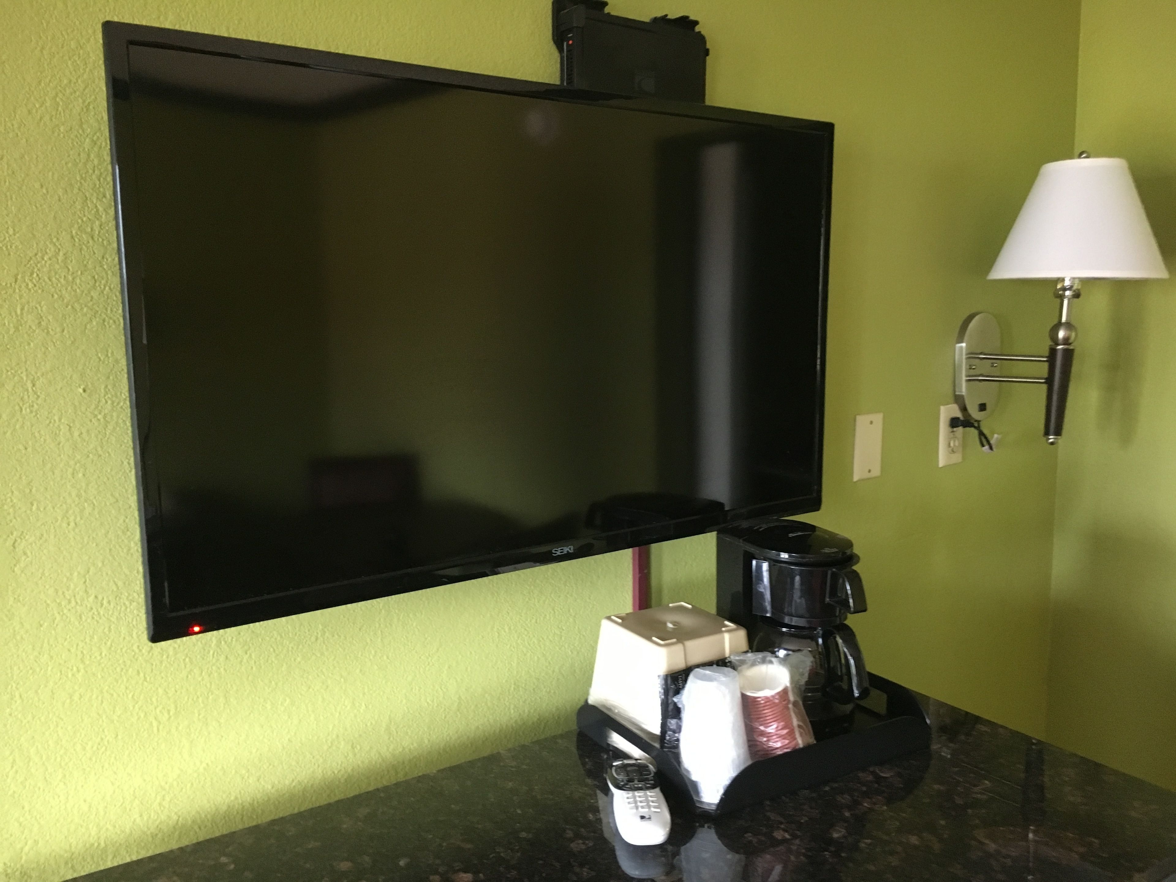 Een kamer met een flatscreen-tv aan de muur, een koffiezetapparaat, een telefoon en een lamp op een aanrecht.