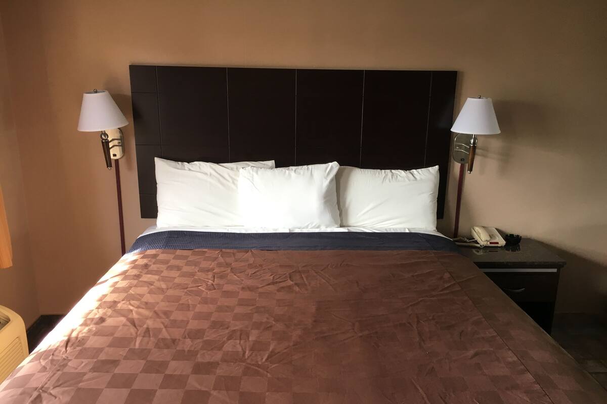 A hotel room with a large bed, two bedside lamps, a nightstand with a phone, and a headboard.