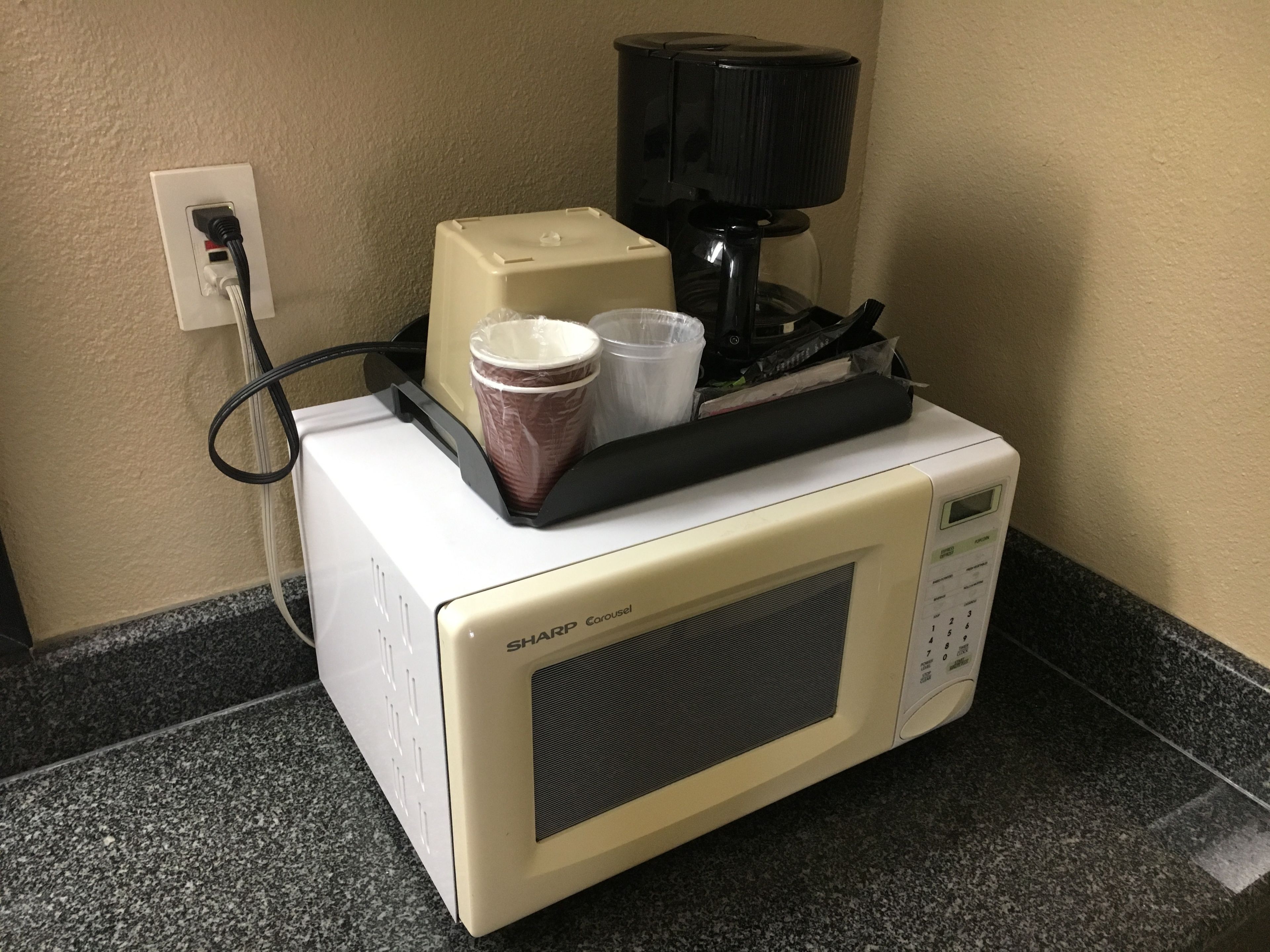 A microwave with a coffee maker and a paper towel dispenser on a granite countertop.