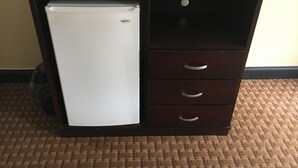 A compact office space with a white refrigerator, a dark wooden desk, and a small drawer unit. - Del Amo Inn (Torrance)