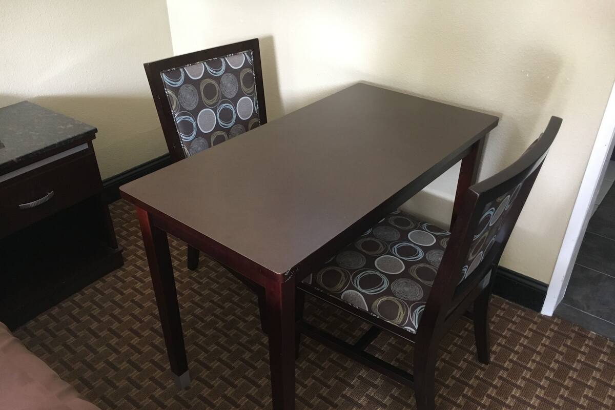 A small, neatly arranged hotel room with a single bed, a wooden table, two chairs, and a small dresser.
