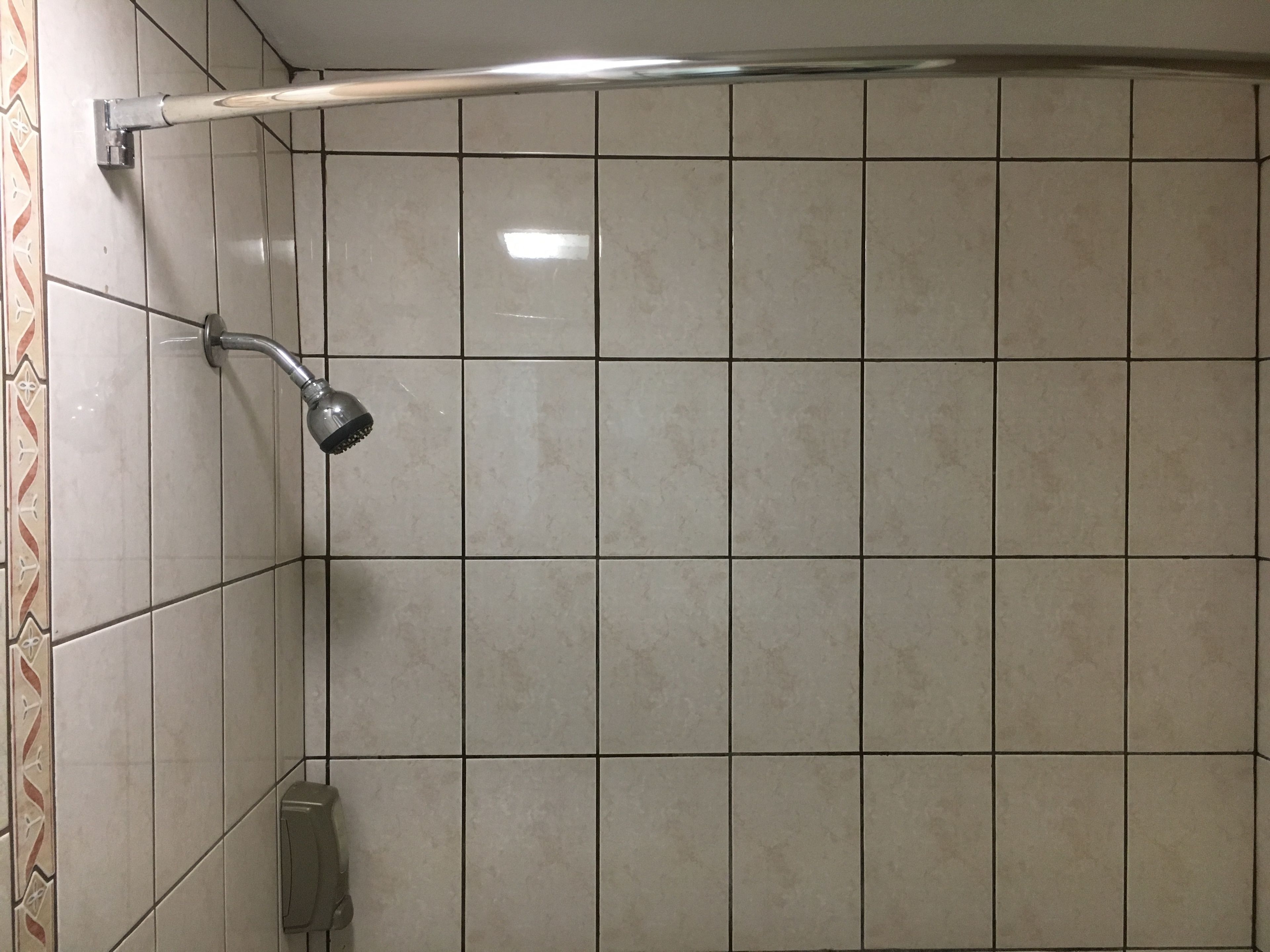 Zona de ducha con azulejos, cabezal de ducha de mano y panel de control en la pared.