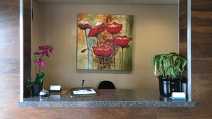 A reception desk with a painting of red flowers, a potted orchid, and a potted plant. - Del Amo Inn (Torrance)