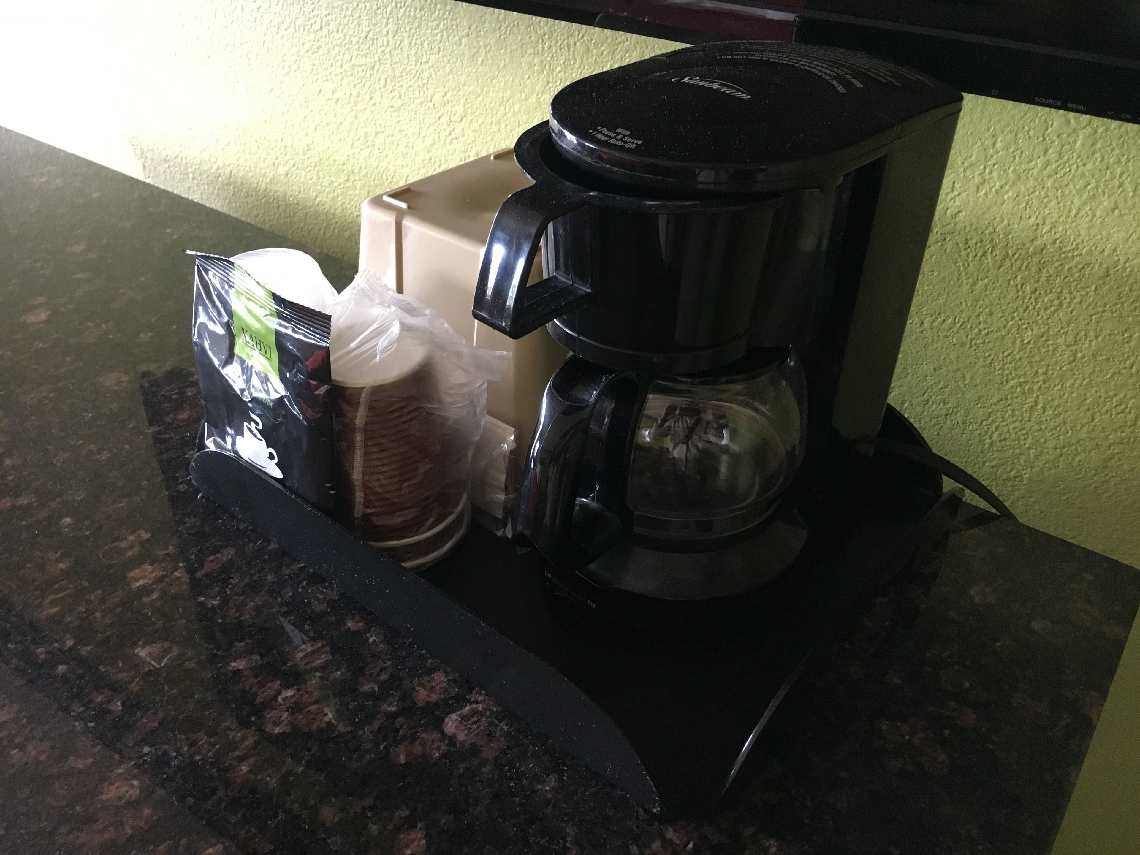 A coffee maker on a kitchen counter with a bag of coffee pods and a container of cream.