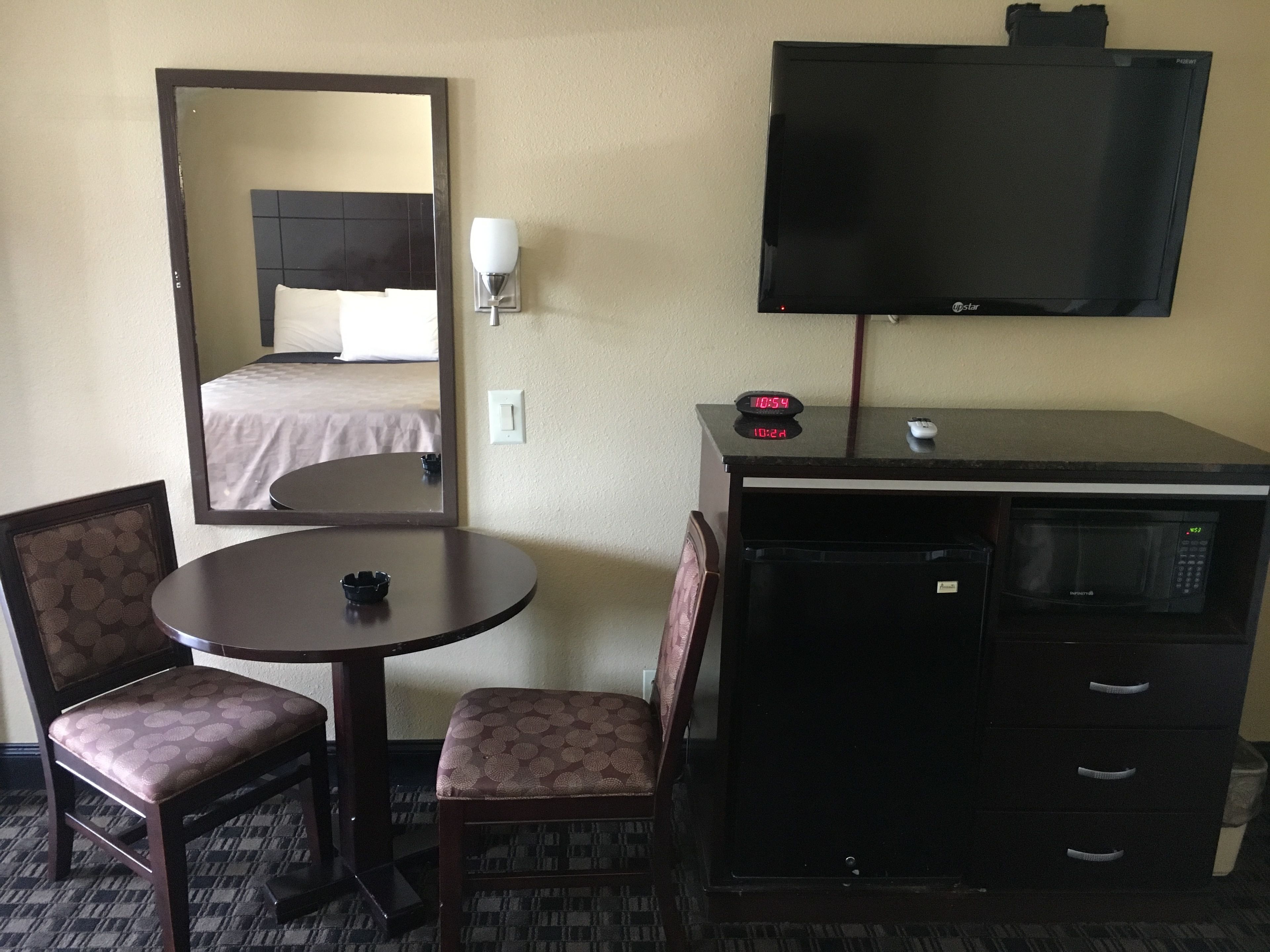 Una habitación de hotel con cama, escritorio con televisor, silla, mesita y microondas.