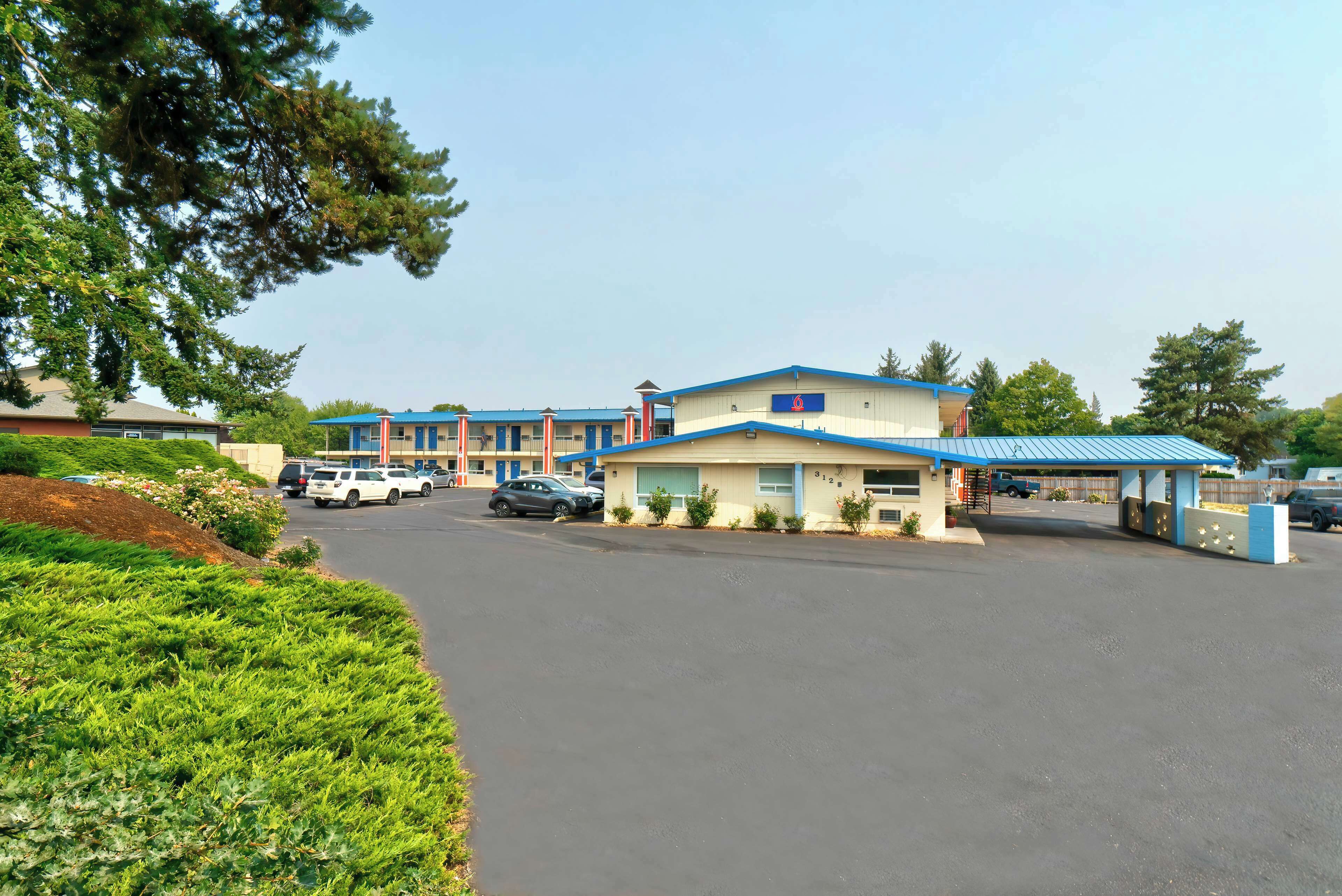 Un motel con estacionamiento, un edificio de techo azul y un pequeño jardín.