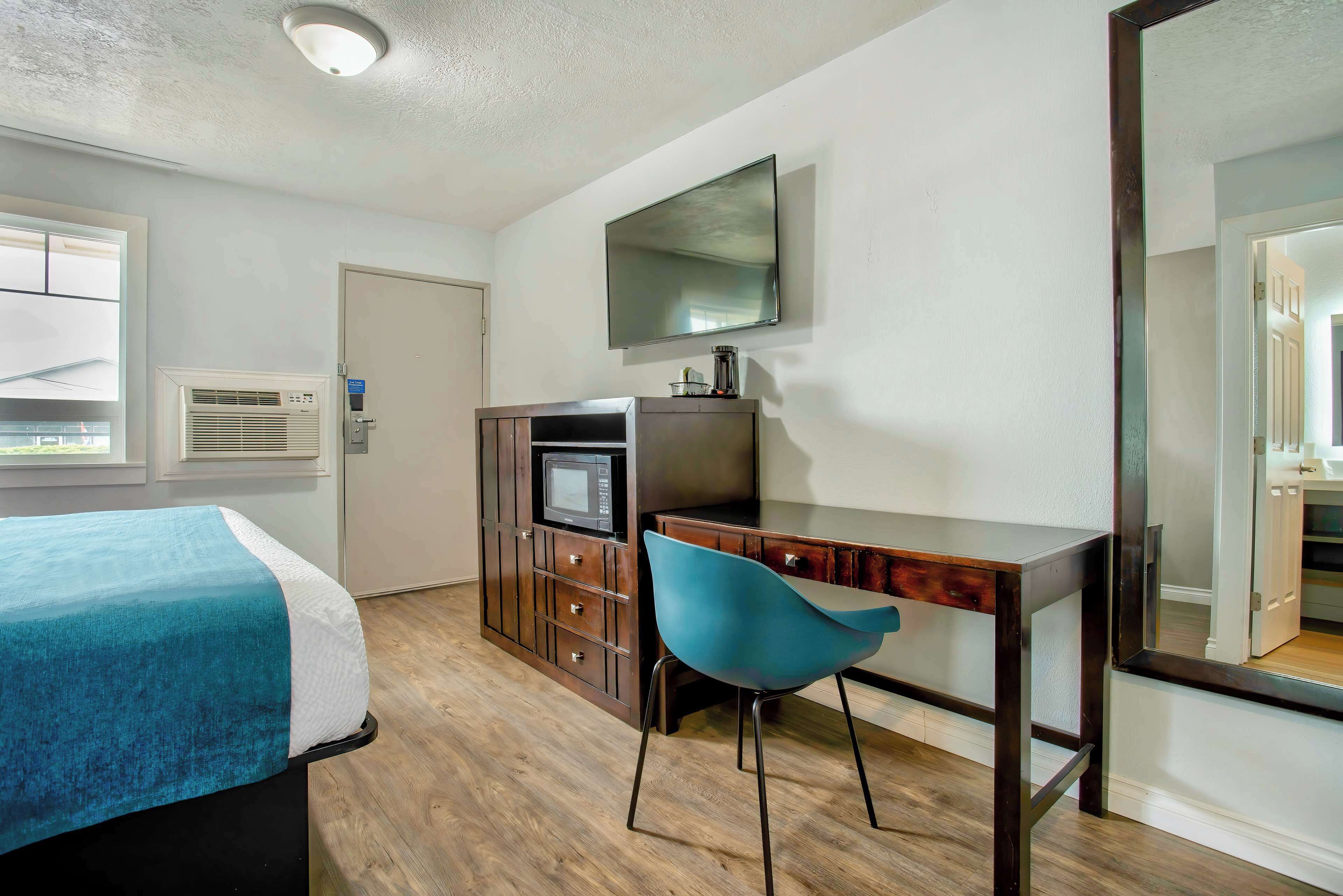 Habitación de hotel con cama, escritorio, silla, televisor y armario.