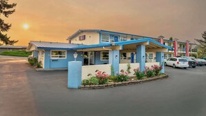 A motel with a blue and beige exterior, a covered parking area, and a row of parked cars. - Studio 6 Suites Albany, OR (Albany)