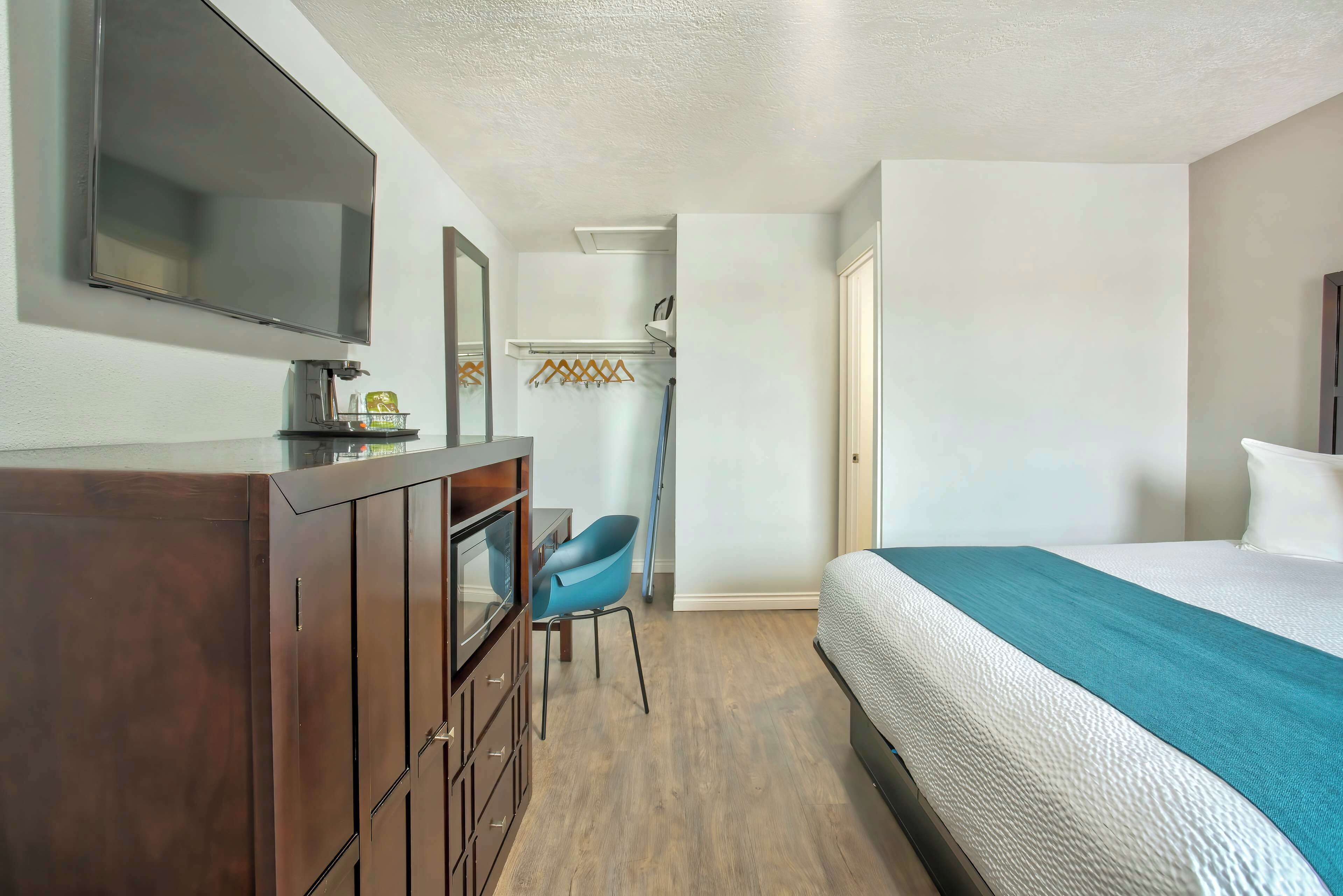 A hotel room with a bed, a desk with a chair, a television, and a wardrobe.