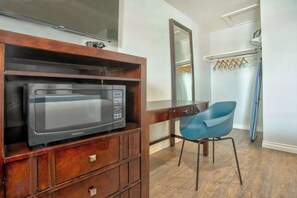 A hotel room with a wooden cabinet, a microwave, a blue chair, a mirror, and a shower area.
