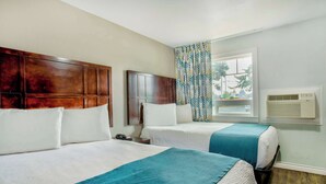 A hotel room with two beds, a wooden headboard, a window with patterned curtains, and an air conditioning unit. - Studio 6 Suites Albany, OR (Albany)