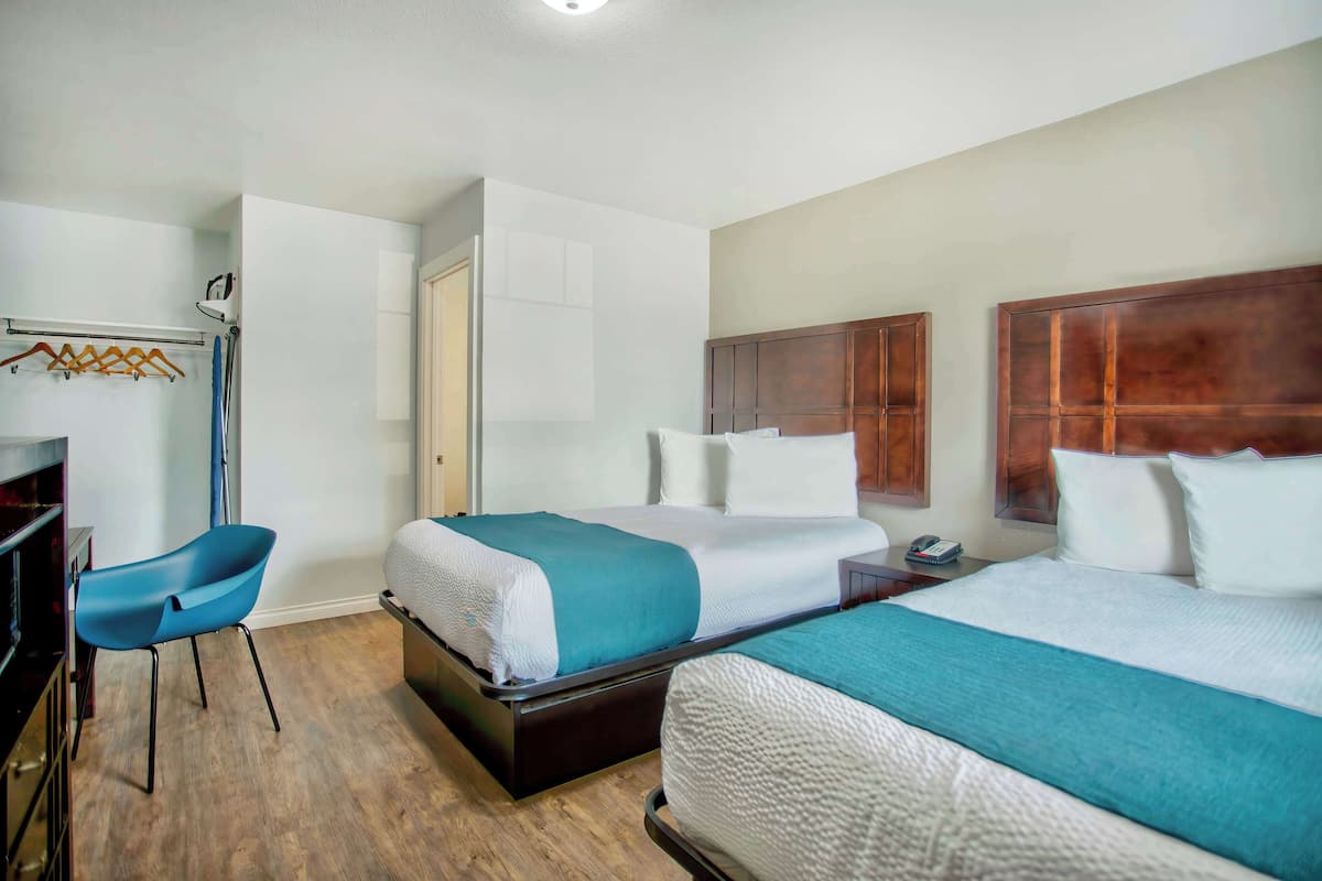A hotel room with two beds, a desk, and a chair.