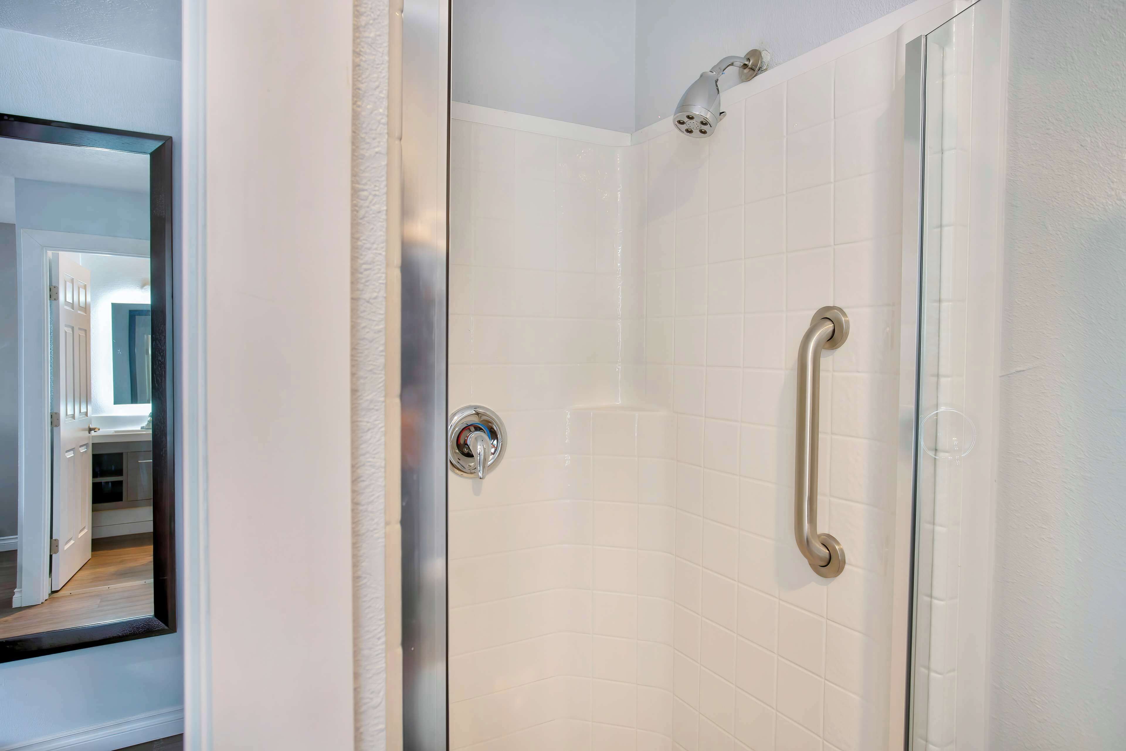 Een badkamer met witte betegelde wanden, een douchecabine van glas en een deur met een zilveren handvat.
