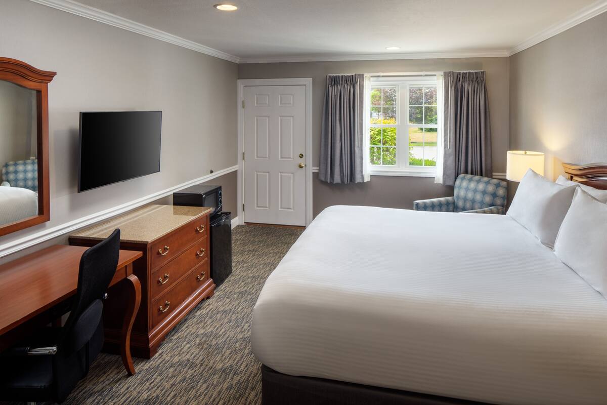 A hotel room with a large bed, a desk with a chair, a television, and a window with curtains.