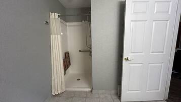 A bathroom with a shower, a door, and tiled flooring.