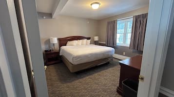 Quarto de hotel com uma cama grande, mesa de cabeceira com luminária, cômoda e janela com cortinas.