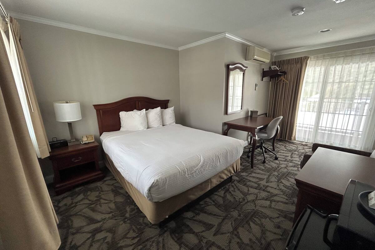 A hotel room with a large bed, a desk, a chair, and a window with curtains.