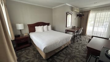 A hotel room with a large bed, a desk, a chair, and a window with curtains.