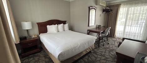 Ein Hotelzimmer mit einem großen Bett, einem Schreibtisch, einem Stuhl und einem Vorhangfenster.