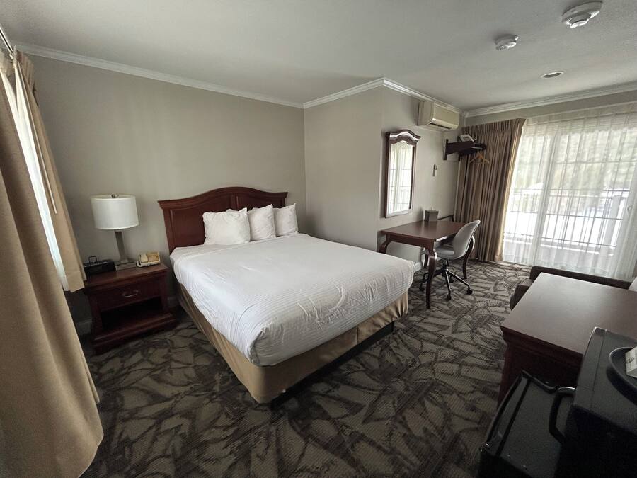 A hotel room with a large bed, a desk, a chair, and a window with curtains.