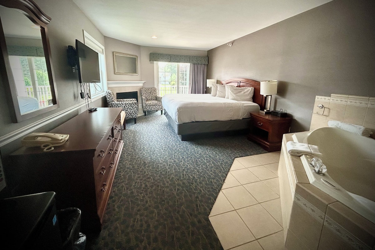 A hotel room with a bed, a desk, a chair, a telephone, a television, a mirror, a fireplace, and a bathtub.