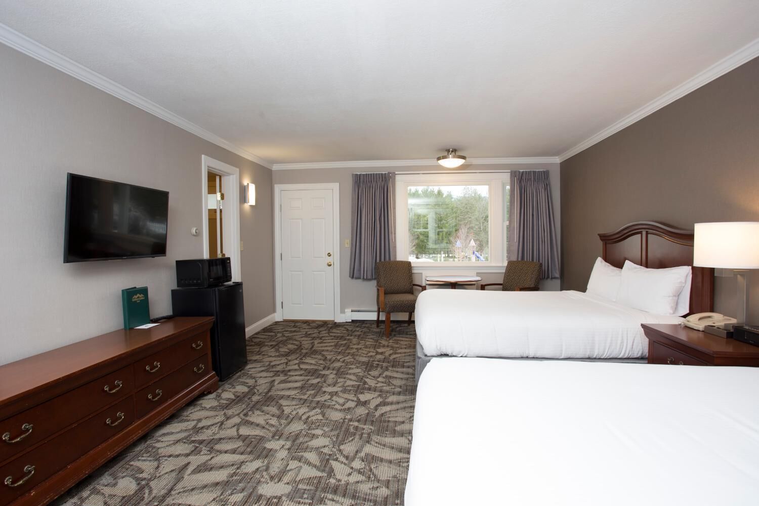 A hotel room with two beds, a TV, a desk with a computer, a chair, and a window with curtains.