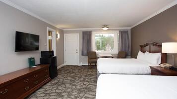 A hotel room with two beds, a TV, a desk with a computer, a chair, and a window with curtains.