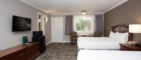 A hotel room with two beds, a TV, a desk with a computer, a chair, and a window with curtains.