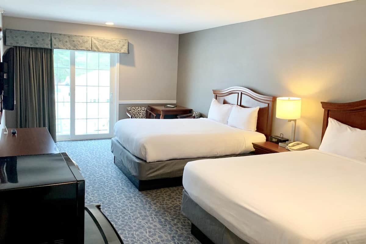 A hotel room with two beds, a desk, a chair, a TV, and a window with curtains.