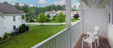 A covered porch with white railings and two white plastic chairs.