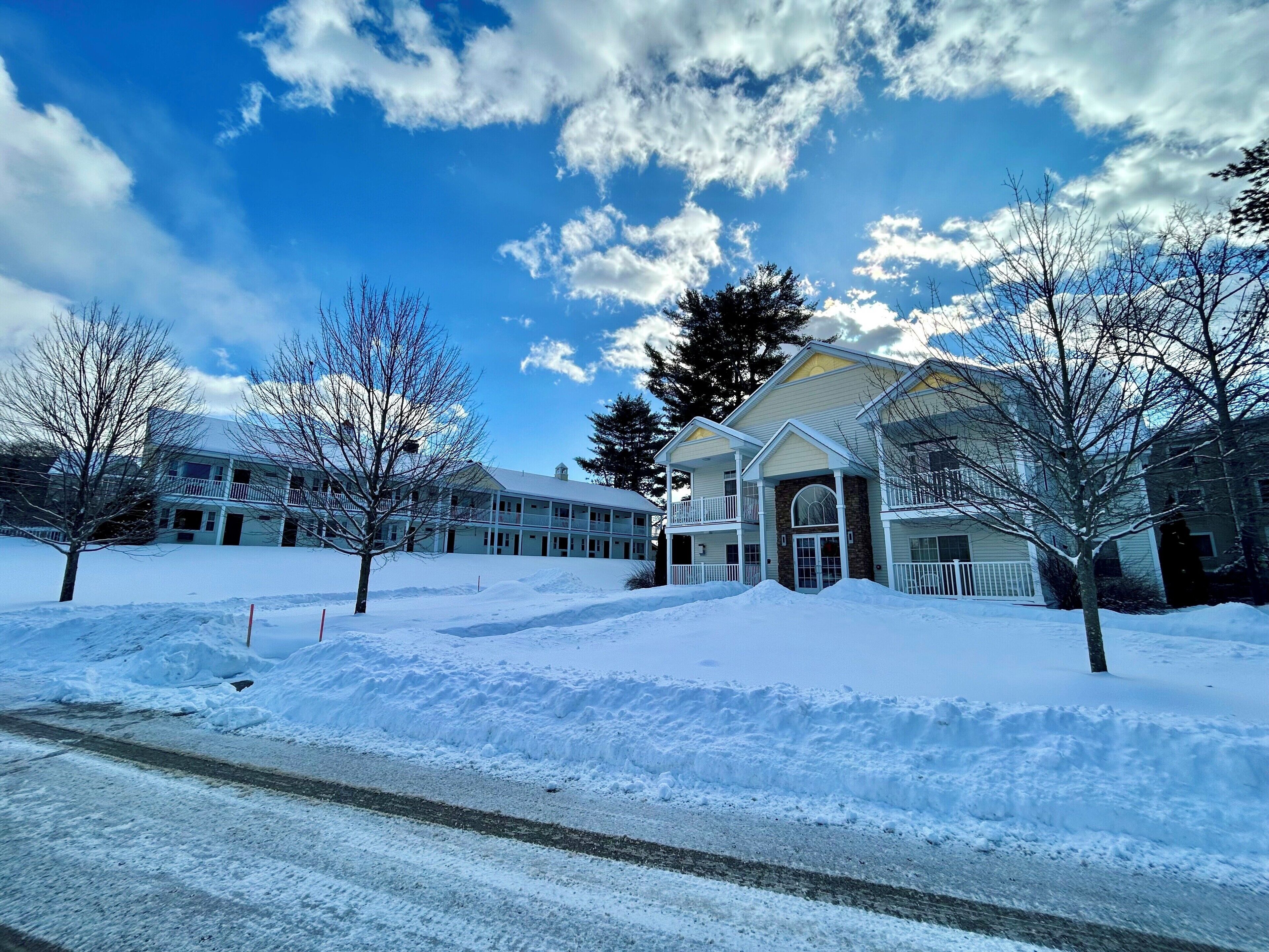 A large, multi-story building with a snow-covered landscape, a clear sky, and bare trees.