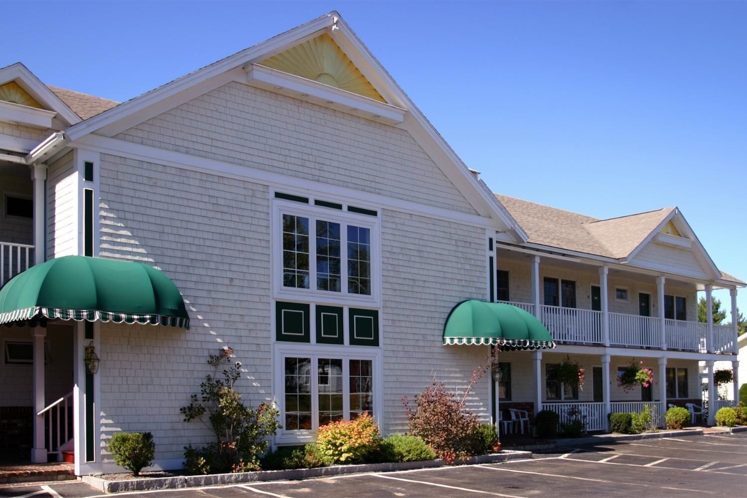 A two-story building with a white exterior, large windows, and green awnings.