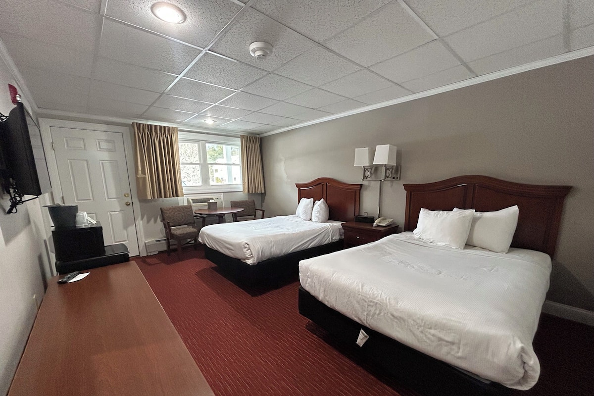 A hotel room with two beds, a desk, a chair, a TV, and a window with curtains.