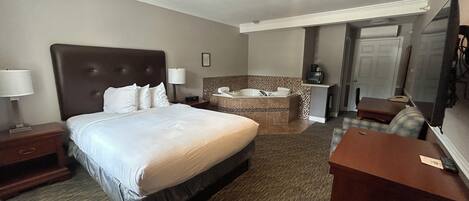 Une chambre d’hôtel dotée d’un grand lit, d’un coin salon avec un bureau, d’une salle de bain avec baignoire et d’un téléviseur.