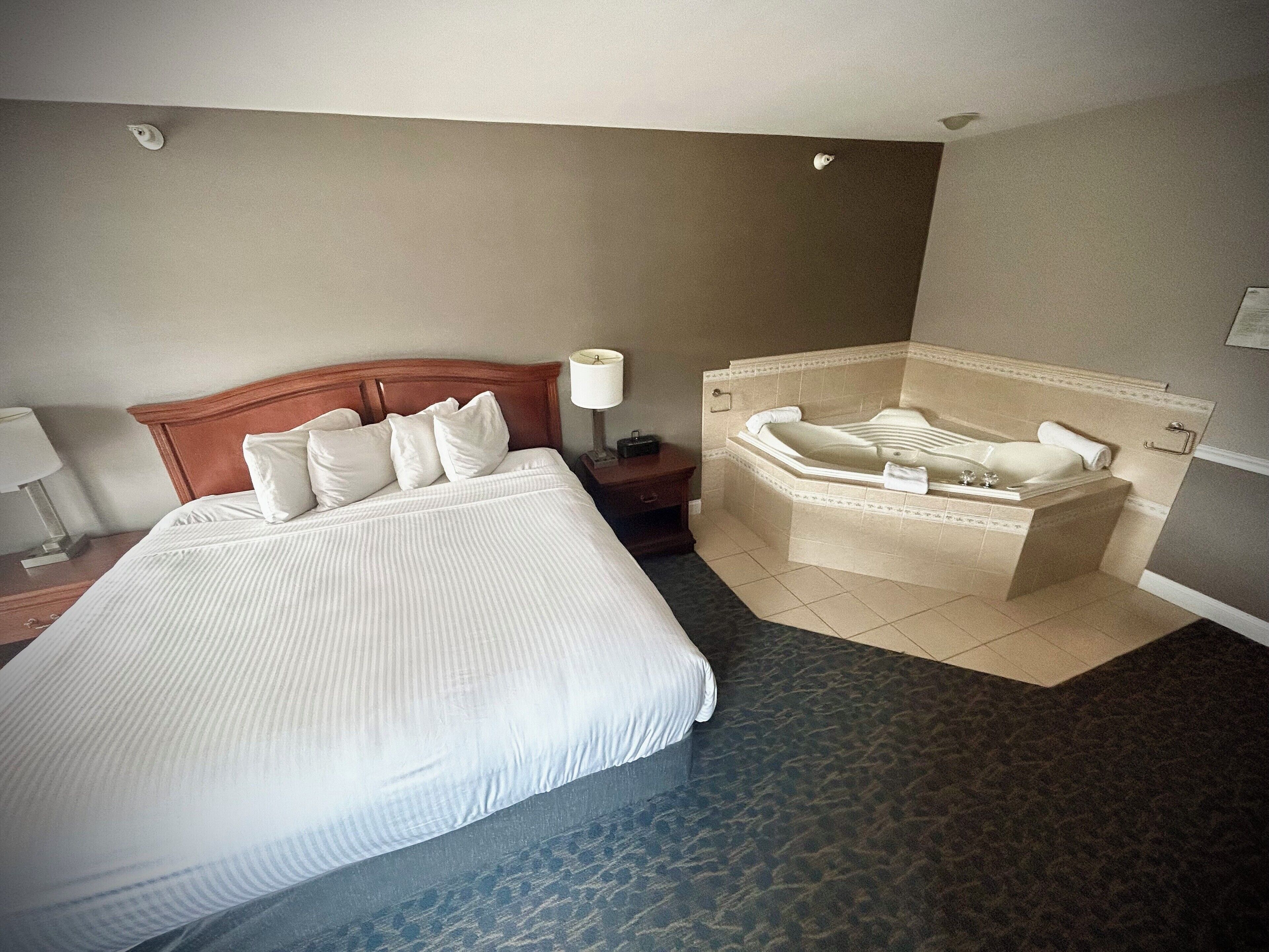 A hotel room with a large bed, a separate bathroom with a bathtub, and a nightstand with a lamp.