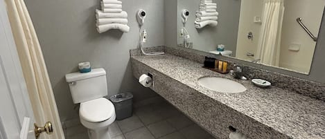 Un baño con inodoro, lavamanos y espejo. Hay toallas colgadas en la pared y una cortina de ducha.